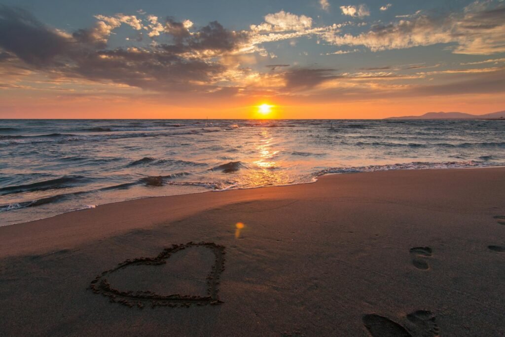 alt="Image of heart drawn in the sand during sunset"