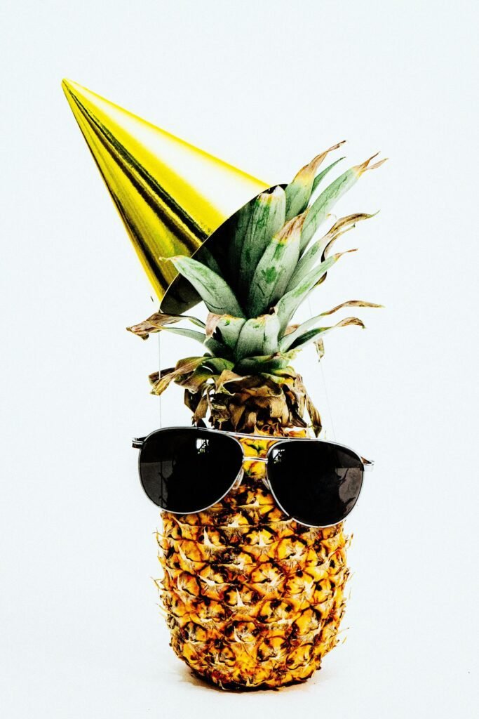 alt="Image of pineapple with sunglasses and a party hat"