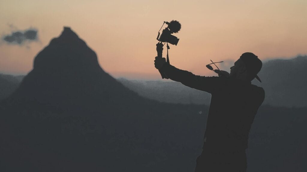 alt="Man holding selfie stick with camera"