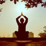 alt=”Image of Figure meditating at sunset”