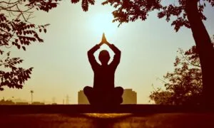 alt=”Image of Figure meditating at sunset”