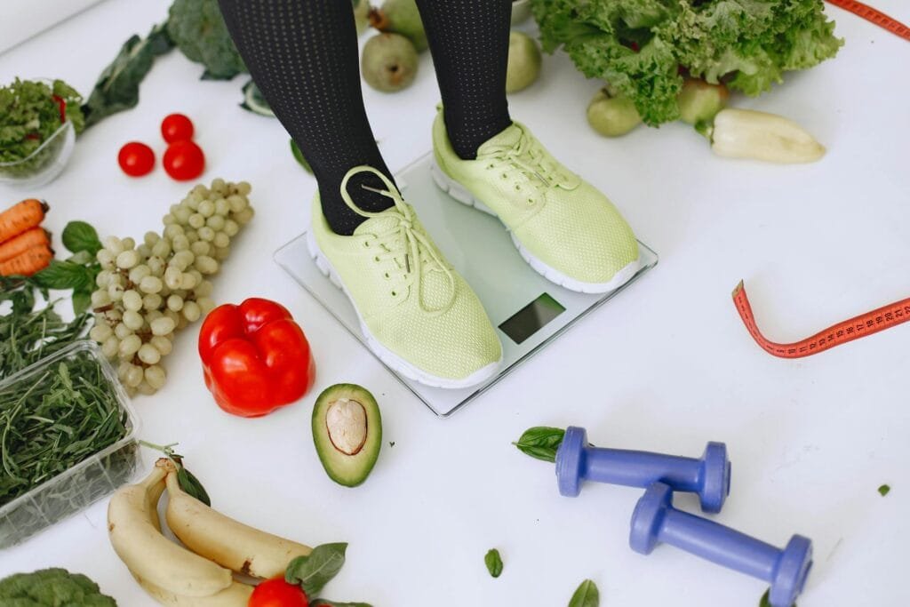 alt="Image of Person standing on scale next to fruits and vegetables"