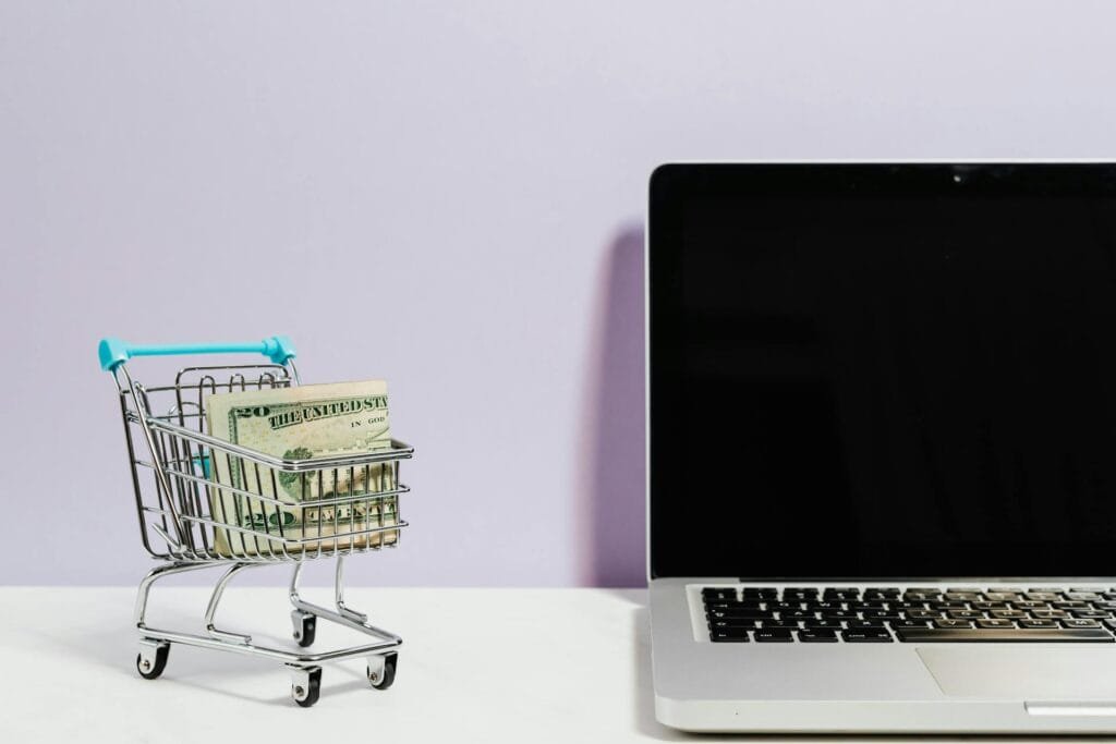 alt="Image of Shopping cart with cash next to laptop"