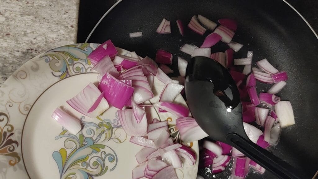 alt="Adding Onions to pan"