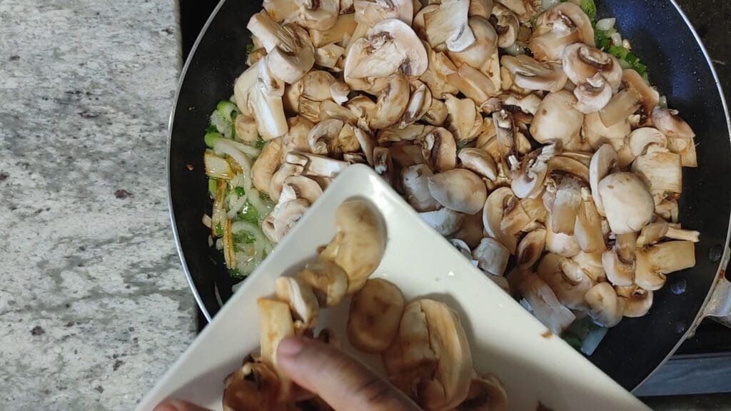 alt="Adding mushrooms to frying pan"