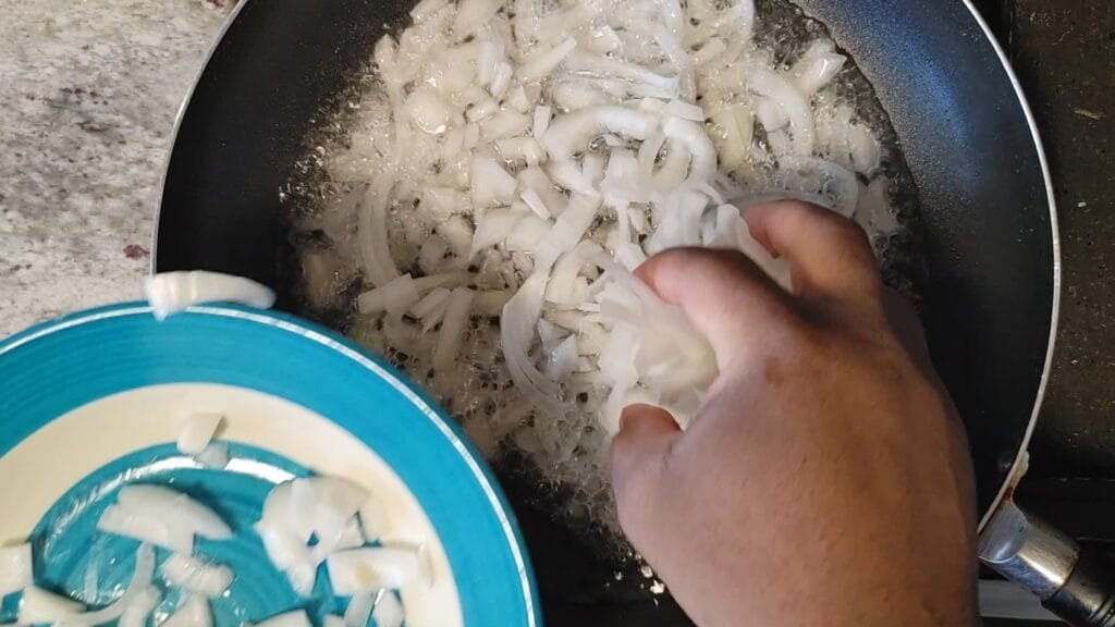 alt="Adding white onions to frying pan"