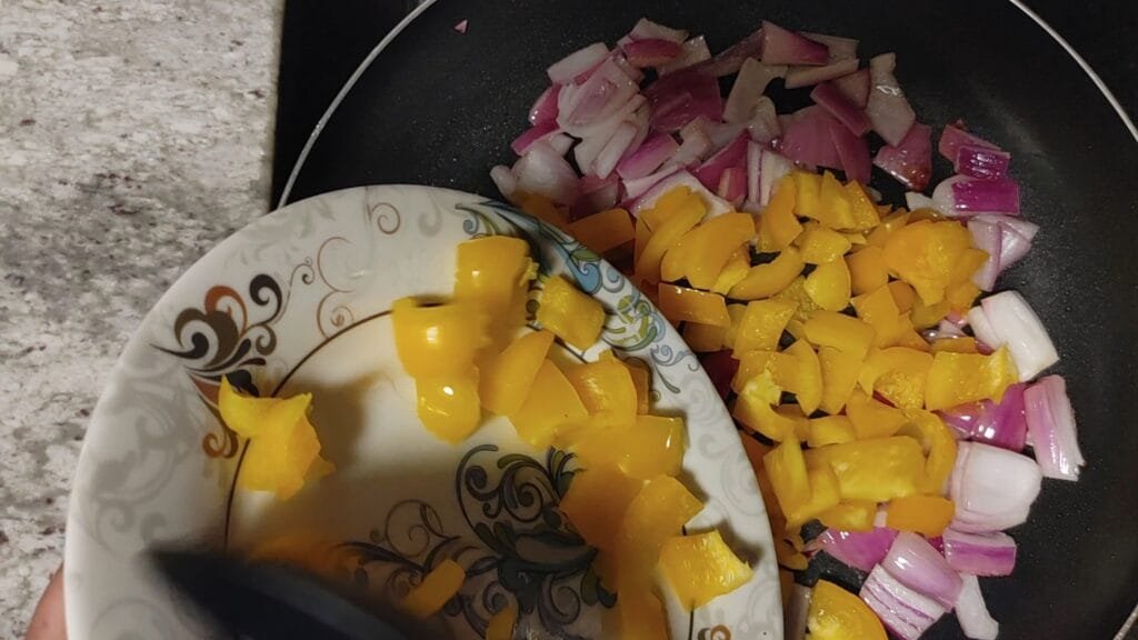 alt="Adding yellow Bell pepper to pan"
