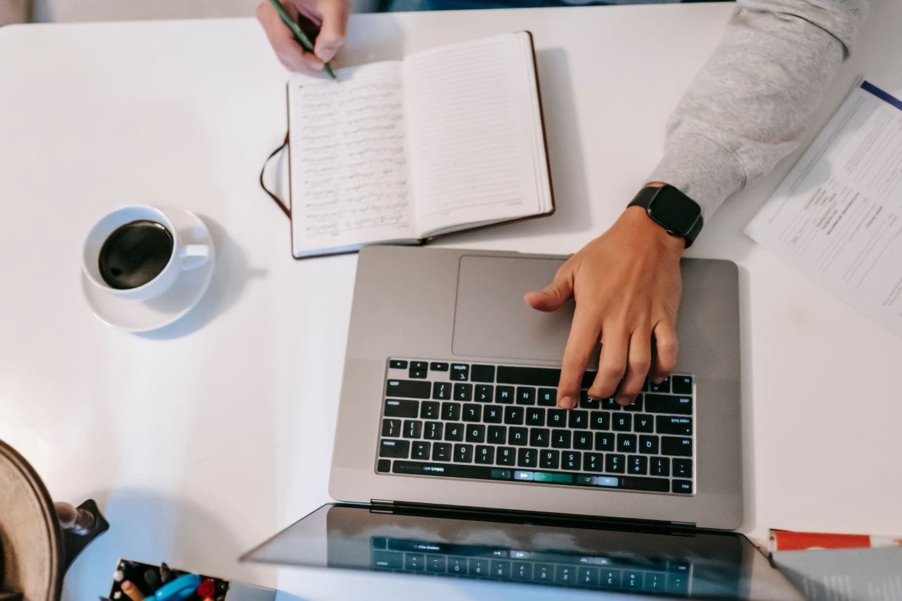 alt="Person using laptop and taking notes"
