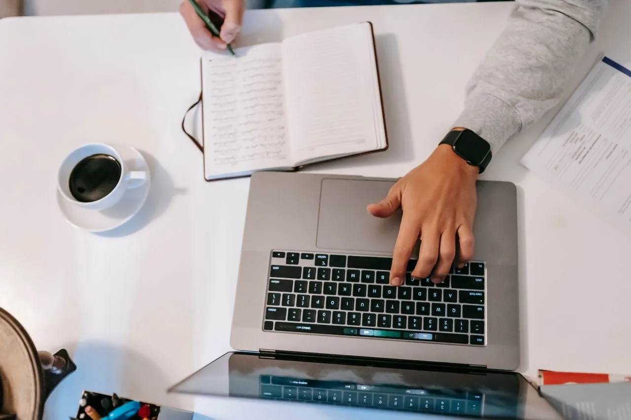 alt="Person using laptop and taking notes"